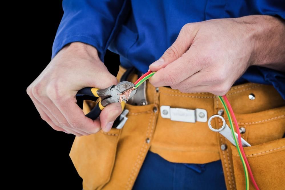 Electrician using pliers to strip wires; wearing blue work shirt and tool belt.