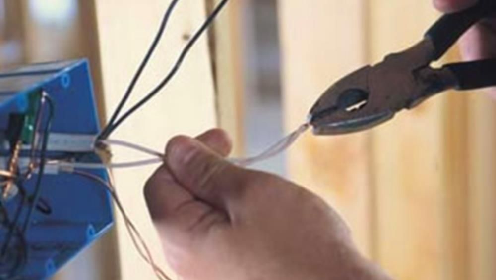 Person using pliers to cut a white electrical wire near a blue electrical box.