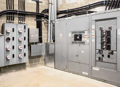 Electrical room with gray metal cabinets, meters, and wiring on brick and concrete walls.