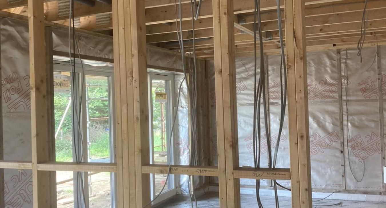 Interior view of a building under construction, showing wooden framing, electrical wiring, and window openings.