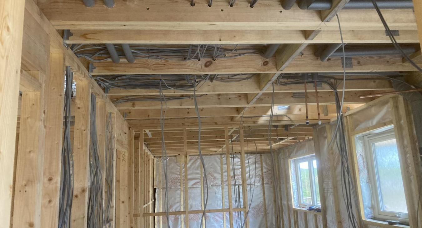 Interior view of a building under construction, showing exposed wooden framing, wiring, and insulation.
