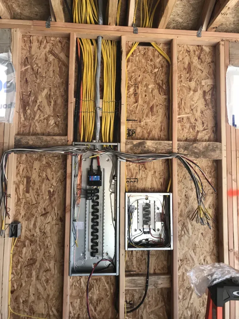 Electrical panel and subpanel installed on a wooden wall, with conduit and wires.