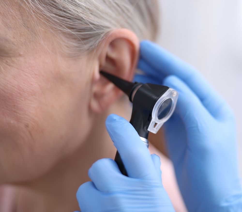 Gloved clinician examining an older person's ear with an otoscope