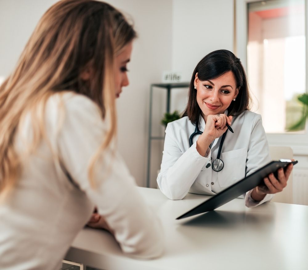 Doctor consulting with a patient in a bright office, holding a tablet and listening attentively.