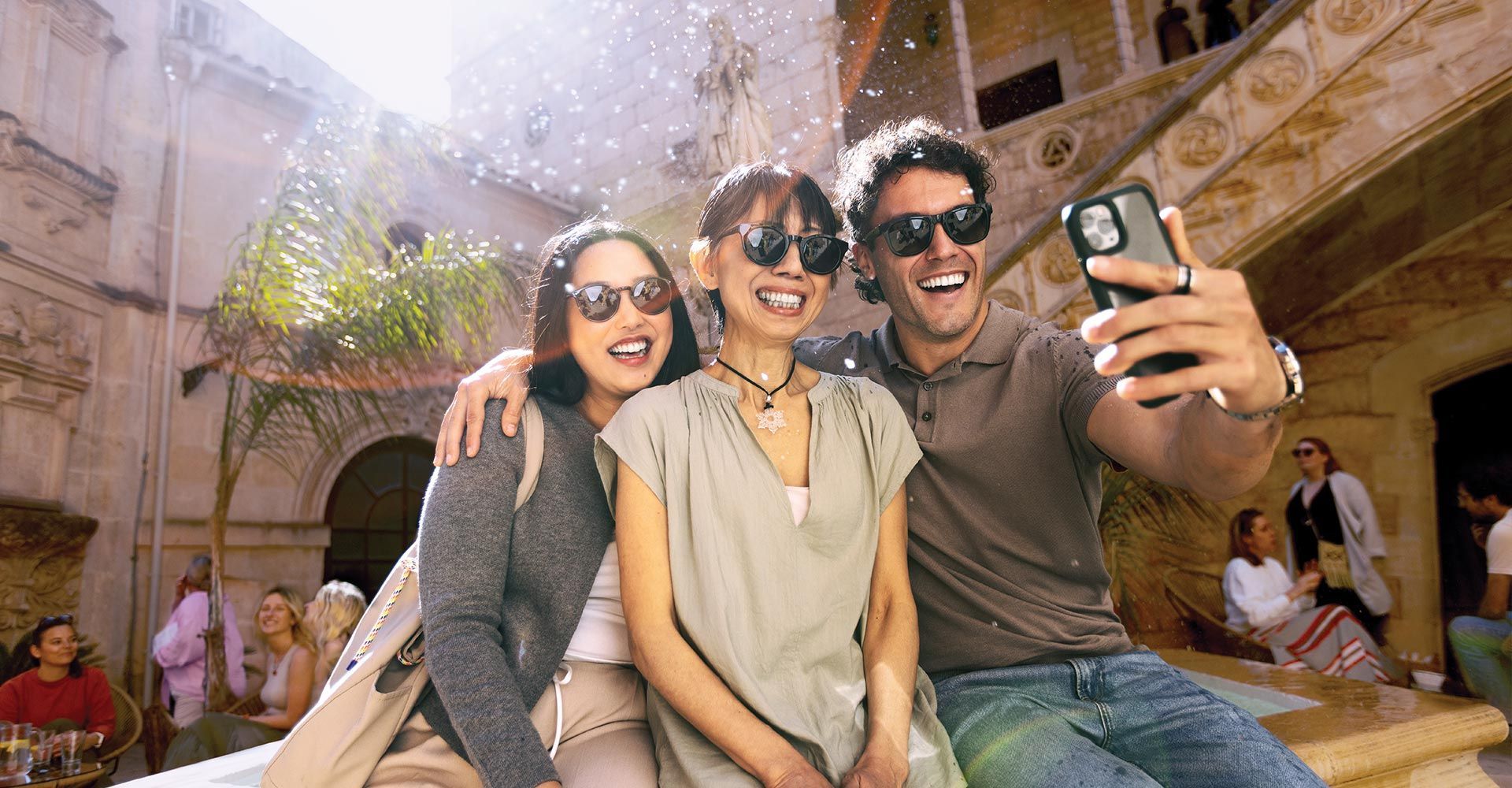 Three friends smiling and taking a selfie together outdoors in bright sunlight