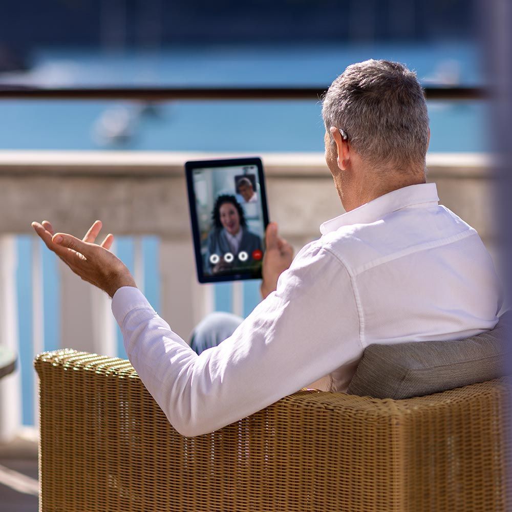 Person on a wicker chair video chatting on a tablet outdoors by the water