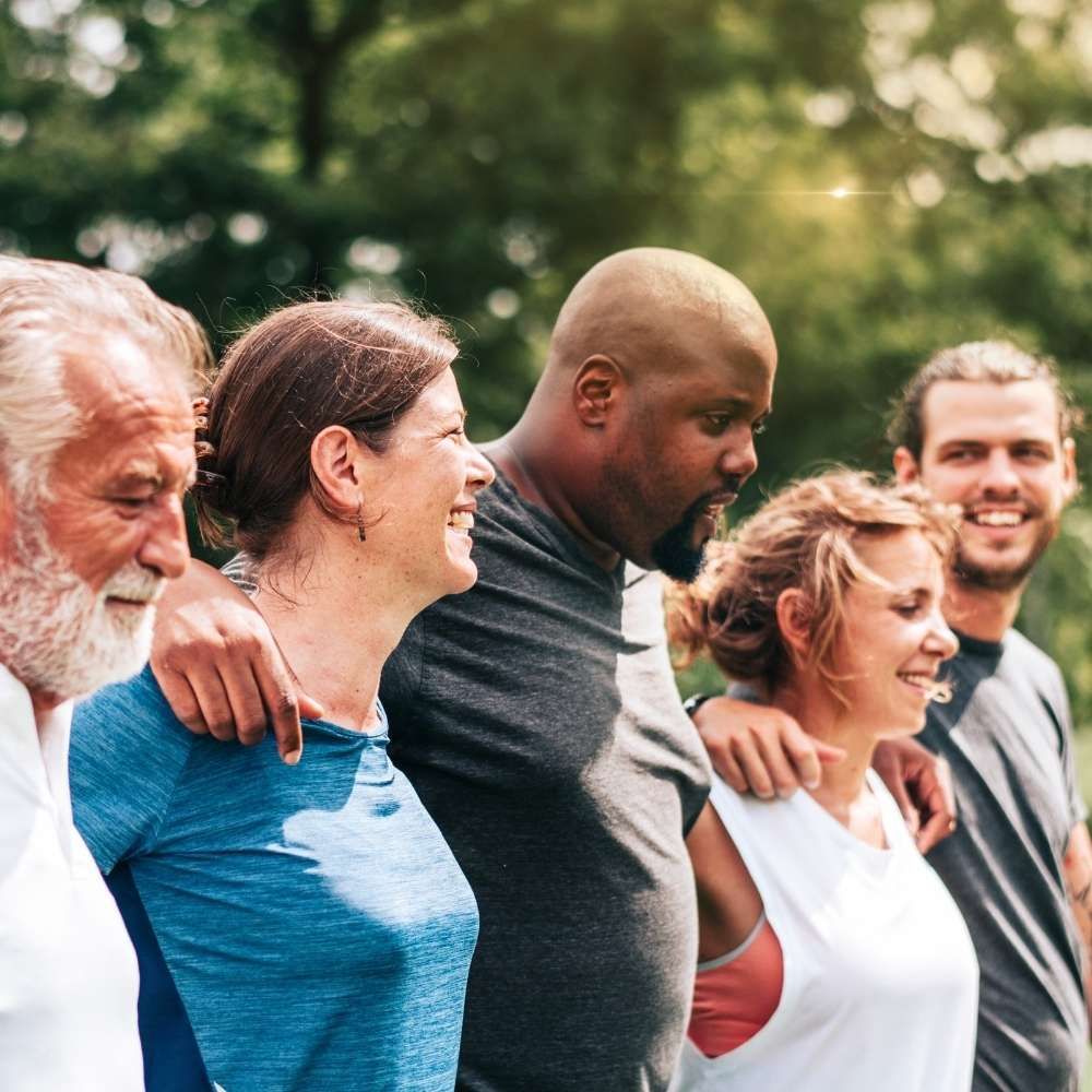 Smiling group walking outdoors with arms around each other in a park