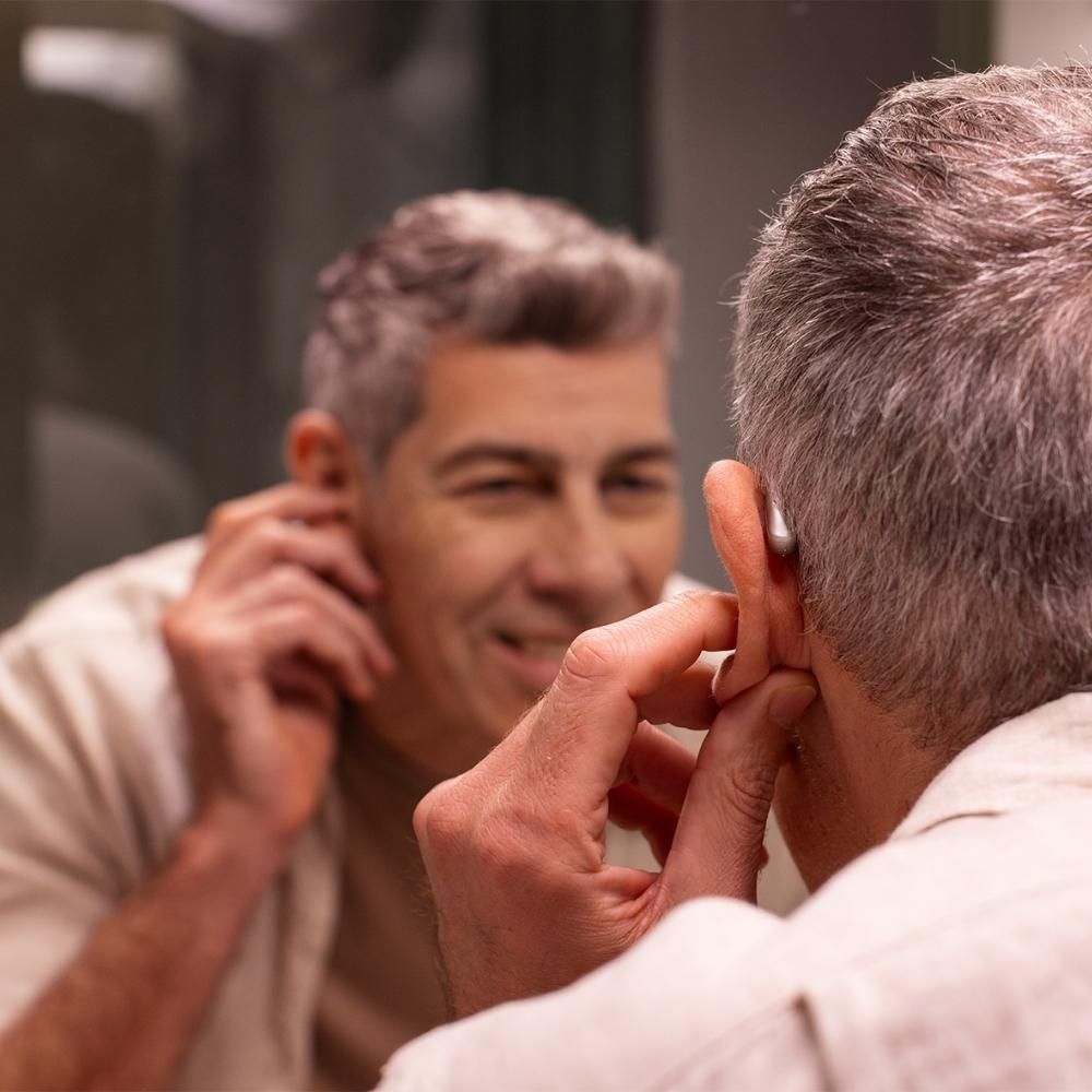 Man adjusting his hearing aid while looking in a bathroom mirror