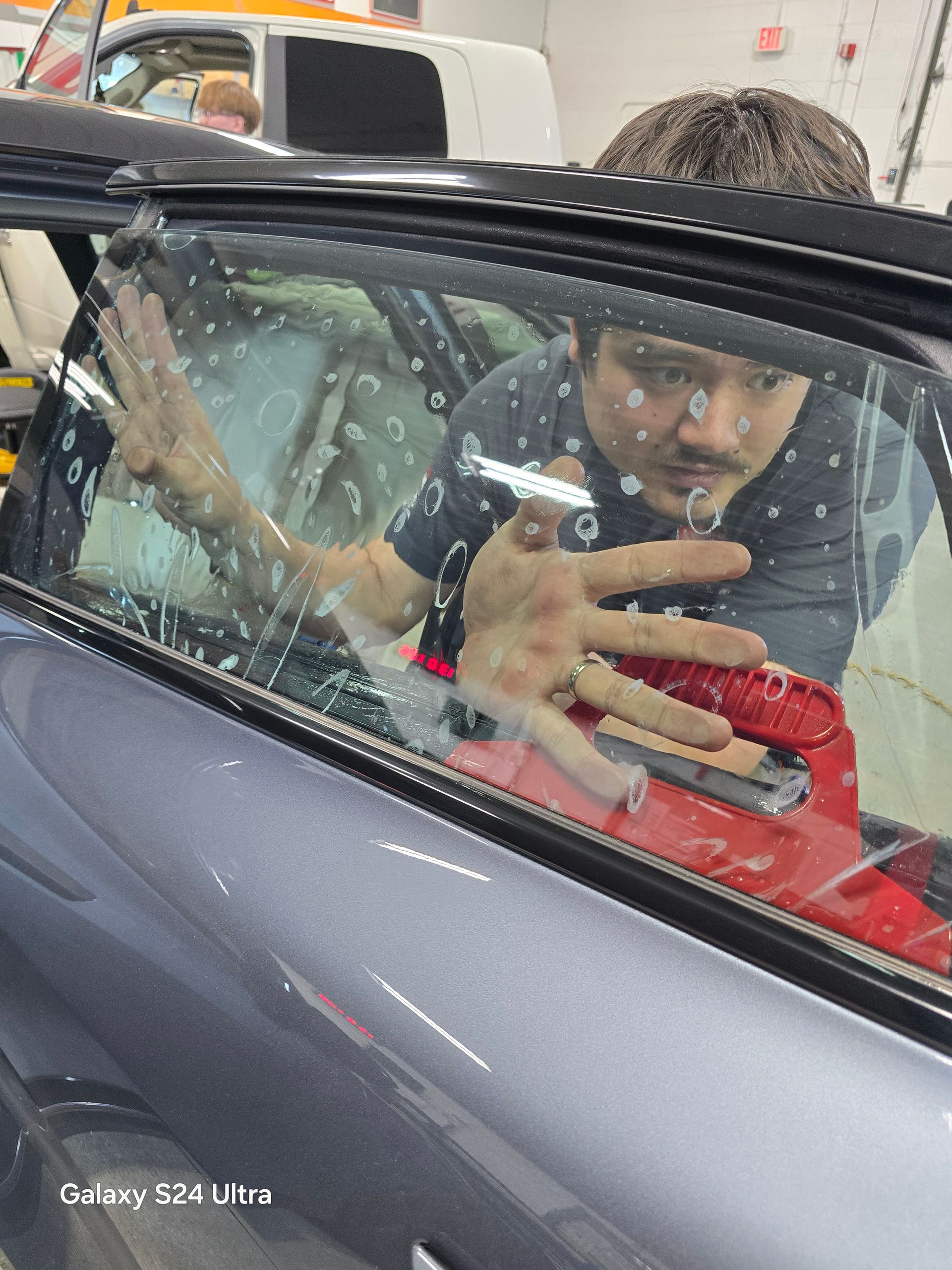 A man is kneeling down in front of a red sports car.