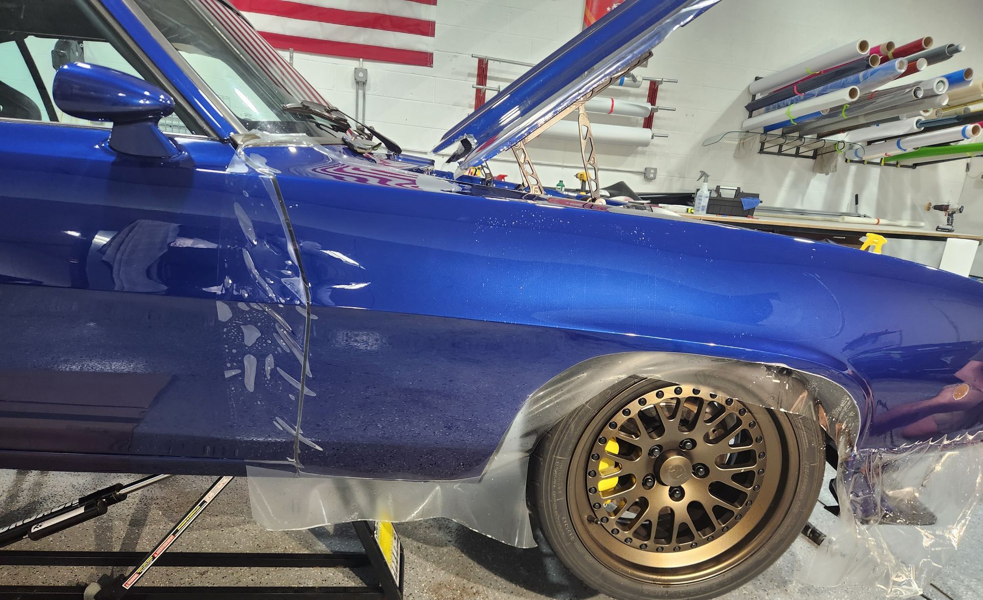 A blue car with the hood up is wrapped in plastic.