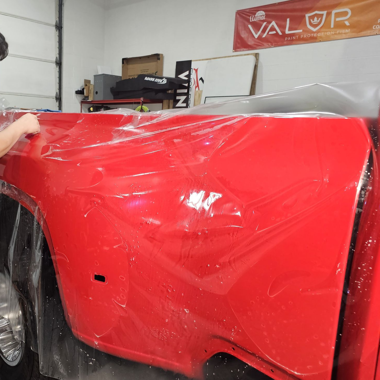 A man is wrapping a red truck in plastic in a garage.