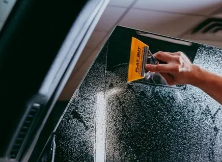 Person using a yellow squeegee to clean a wet car window with soap suds