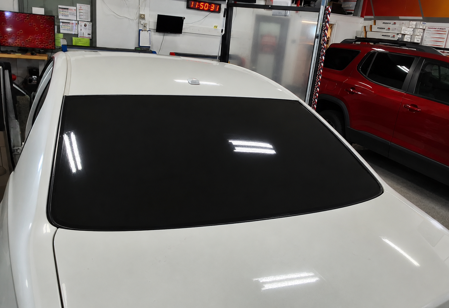 White car in a garage with a black windshield, parked beside a red vehicle