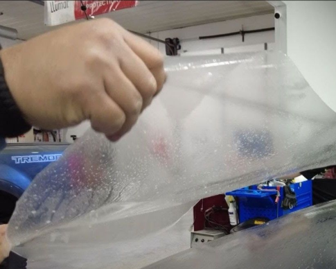 A man is wrapping a car with plastic wrap in a garage.