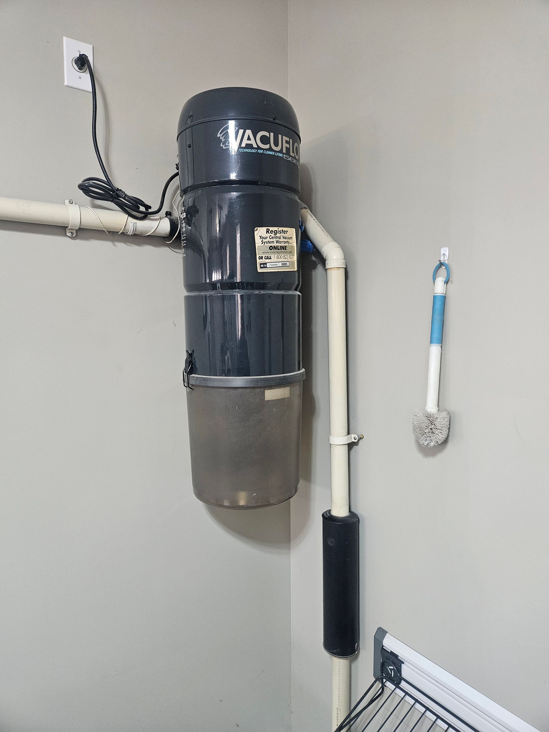 Black and silver central vacuum unit mounted on a beige wall with white pipes.