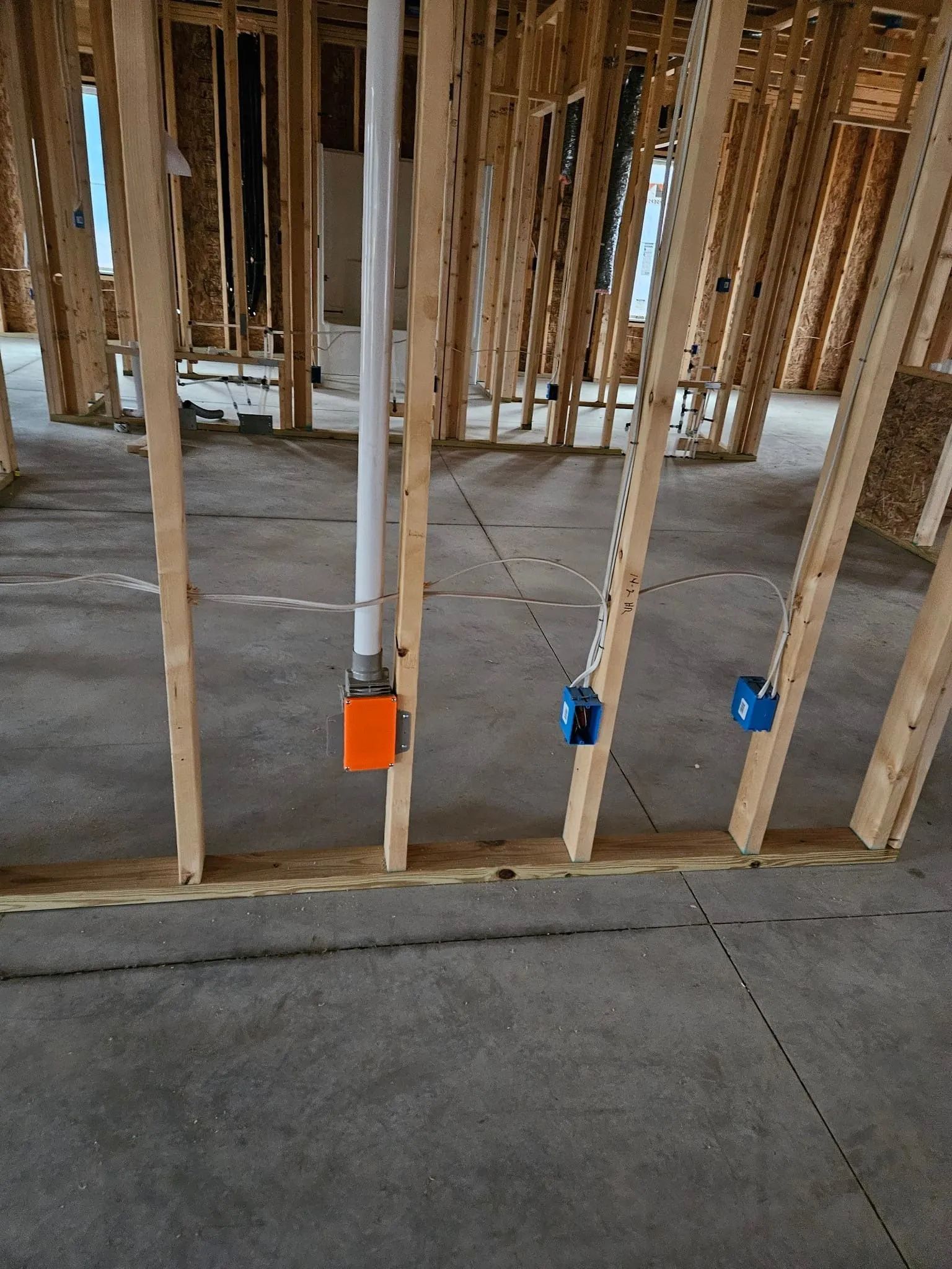 Construction framing with exposed studs and electrical boxes on a concrete floor