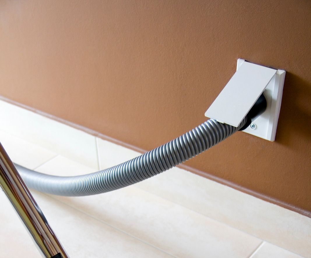 Corrugated gray hose running from wall opening to floor, with a white cover plate on a brown wall