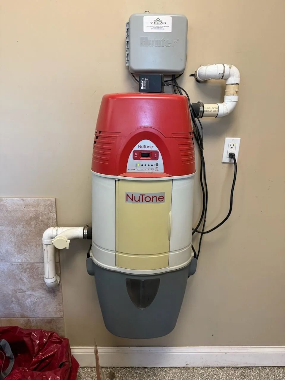 Wall-mounted NuTone vacuum unit with red, cream, and gray casing in a home utility area