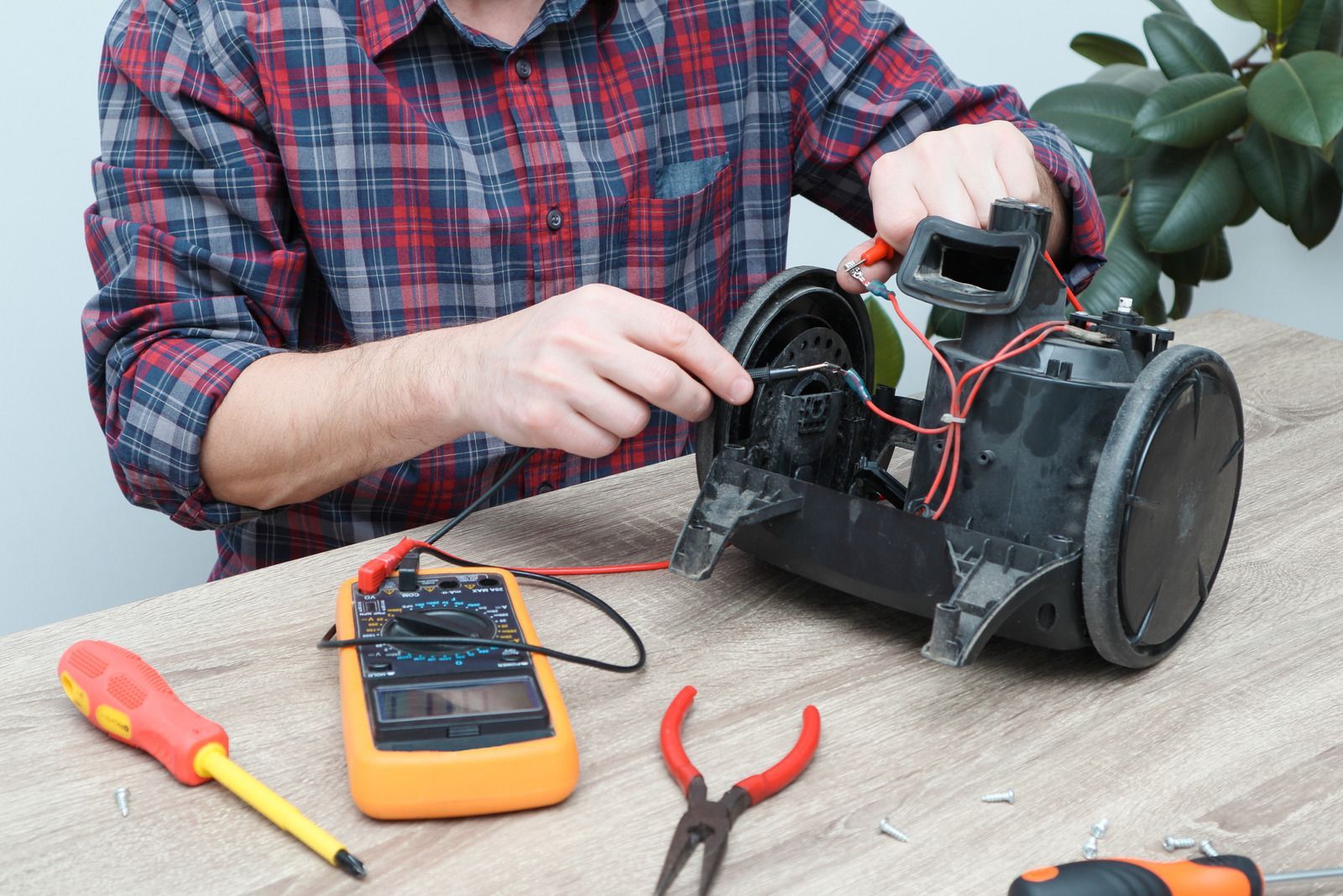 A man is repairing a vacuum cleaner on a wooden table.