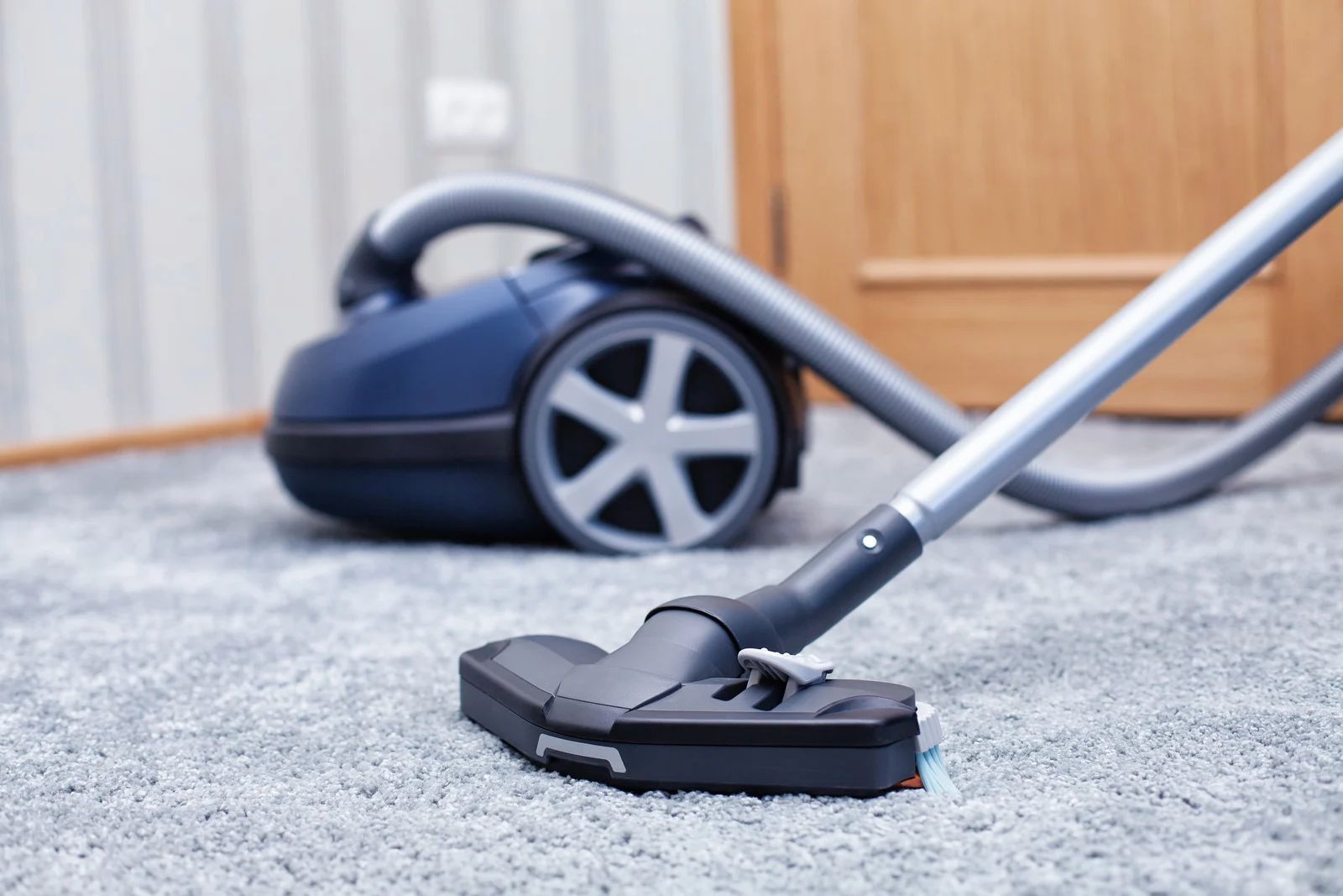 Blue vacuum cleaner on a light gray carpet, cleaning.