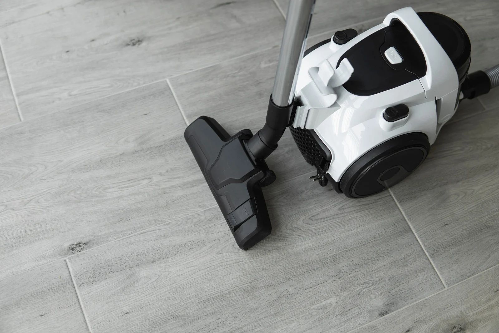 White and black vacuum cleaner on gray tiled floor.