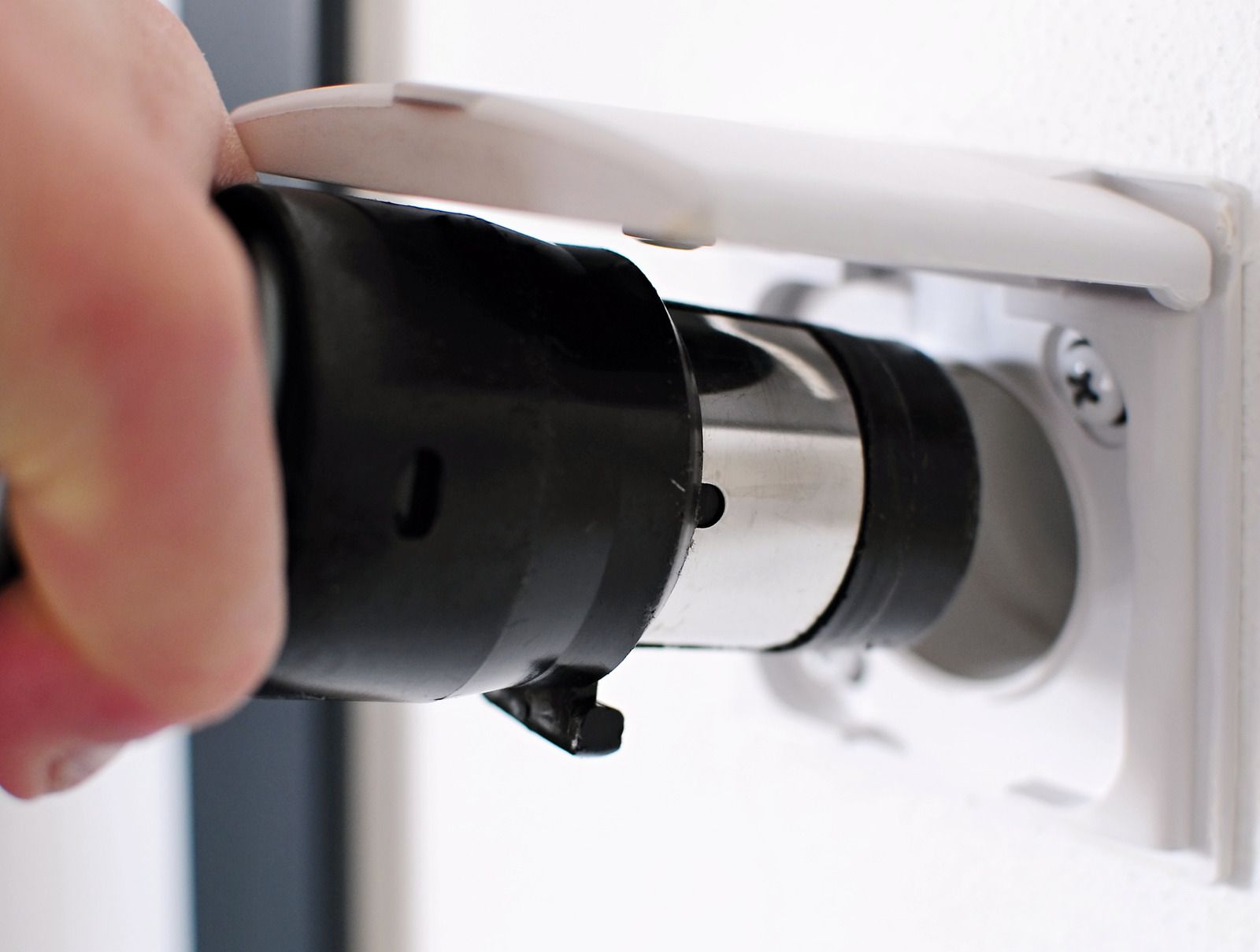 Hand holding a plug near a white wall outlet