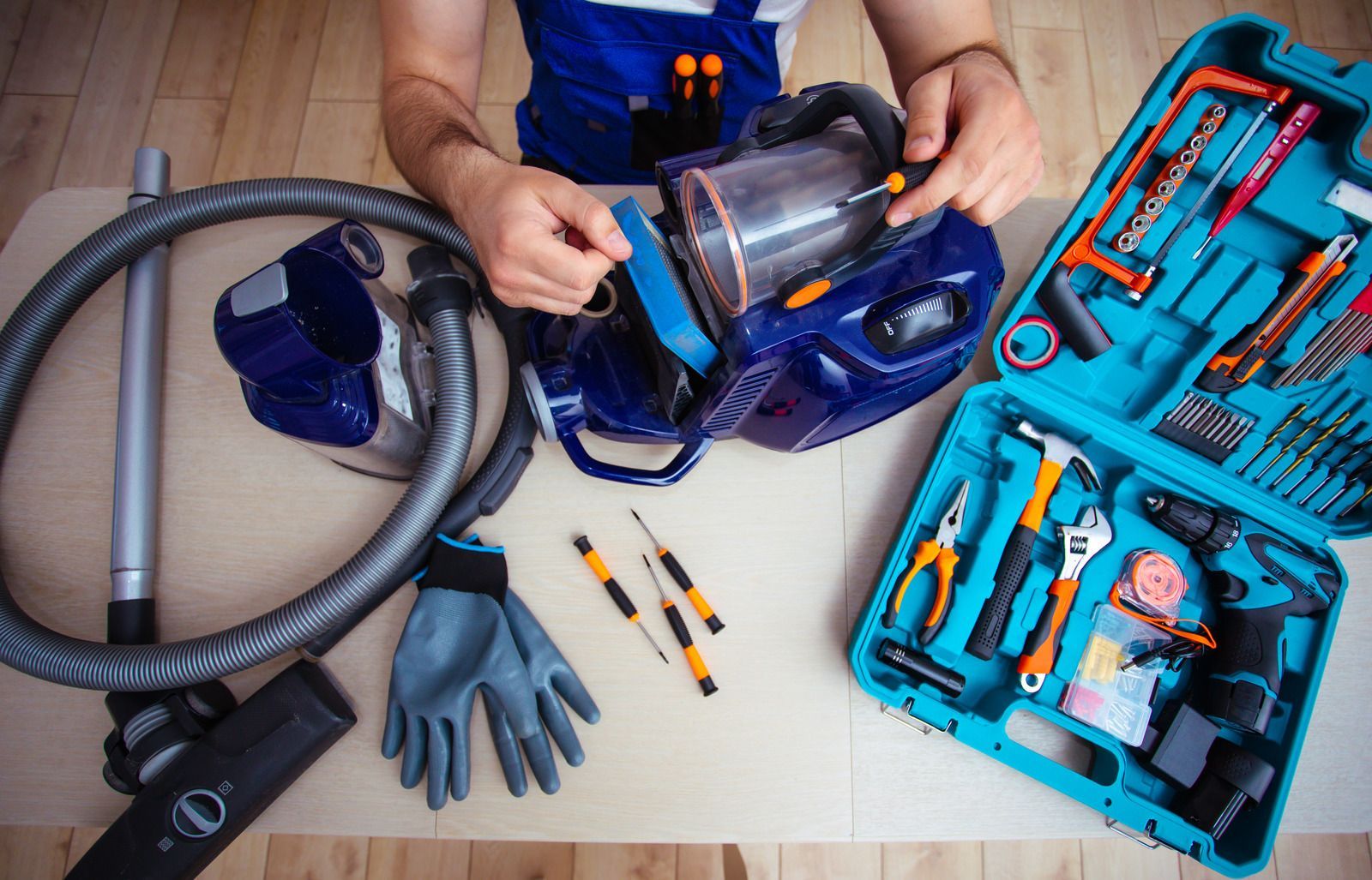 Person repairing vacuum cleaner with tools laid out on a table.