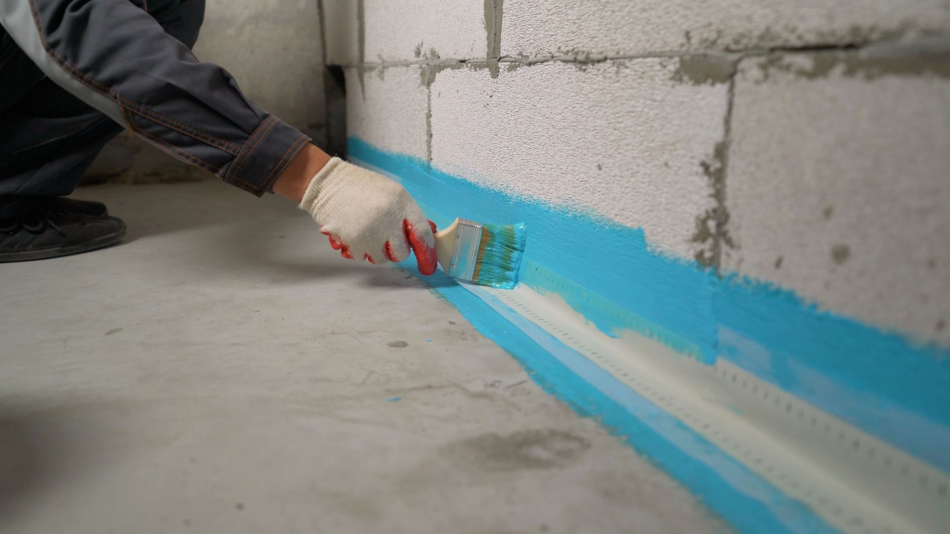 Construction worker applying waterproofing paint on basement wall.