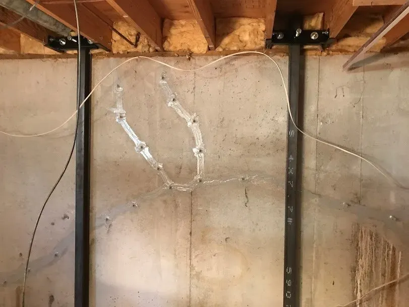 Basement wall with vertical steel beams and a crack. Wires run across the wall and ceiling.