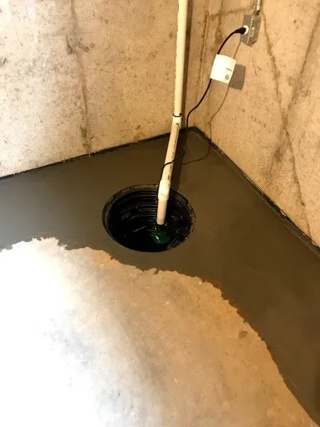 Sump pump pit with a pipe and electrical outlet in a concrete basement.
