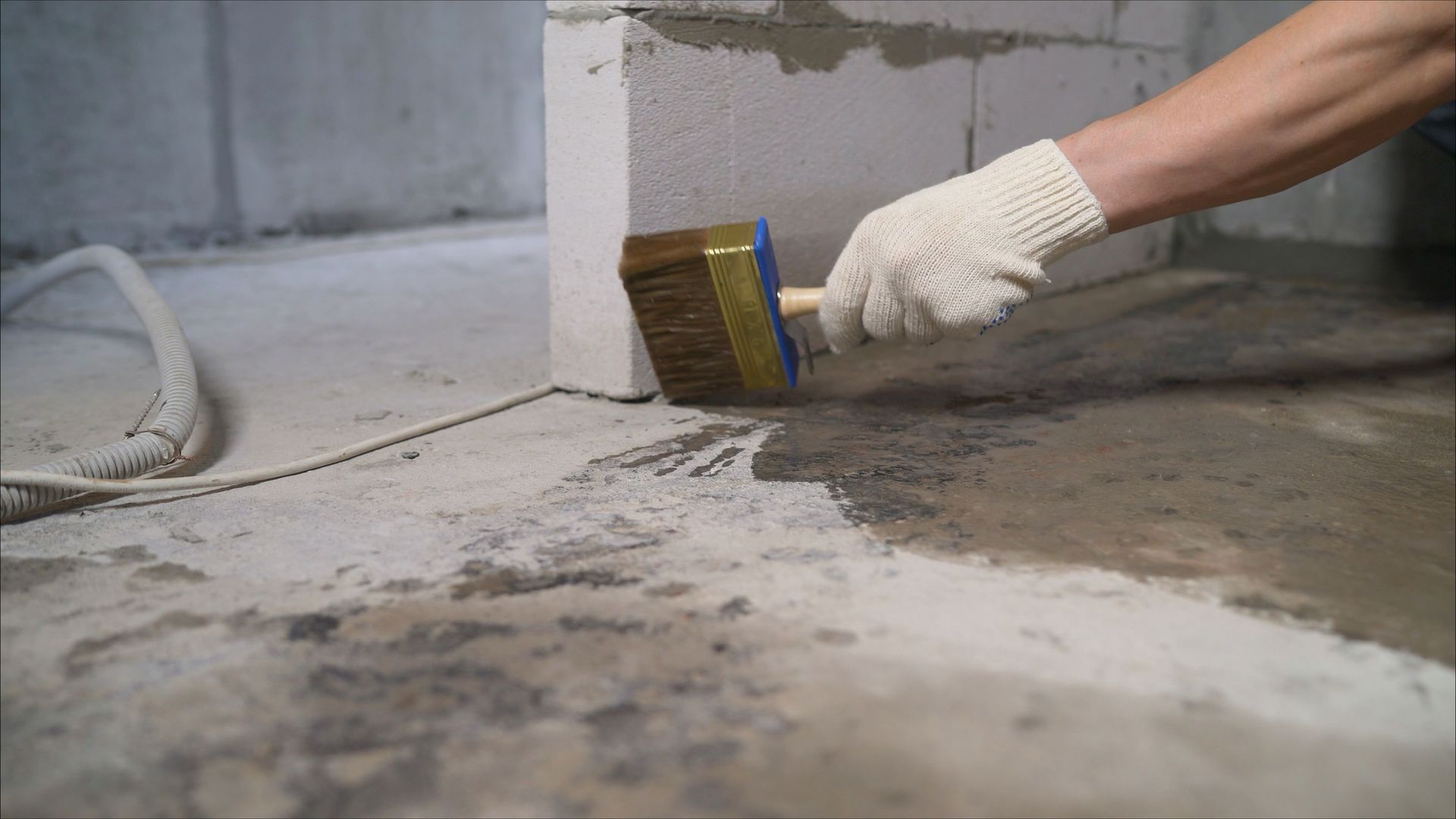 Construction worker applying waterproofing coating on a concrete floor with a brush.