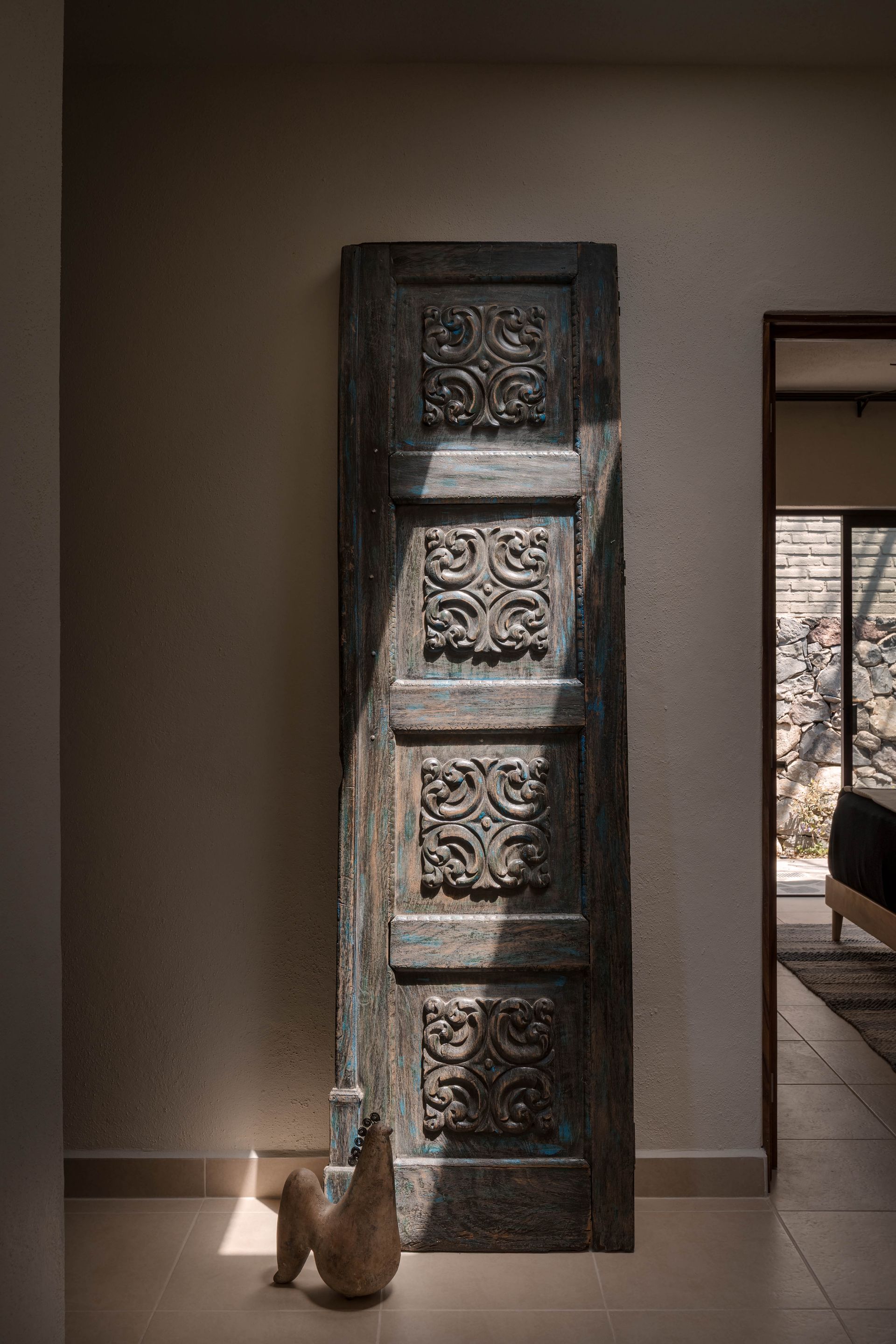 A statue of a chicken is sitting next to a carved wooden door in a hallway.