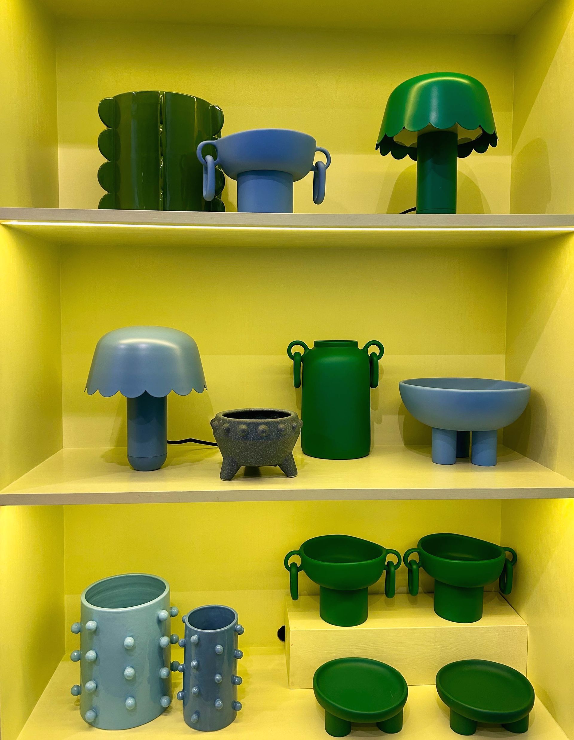 A shelf filled with a variety of green and blue vases and bowls.