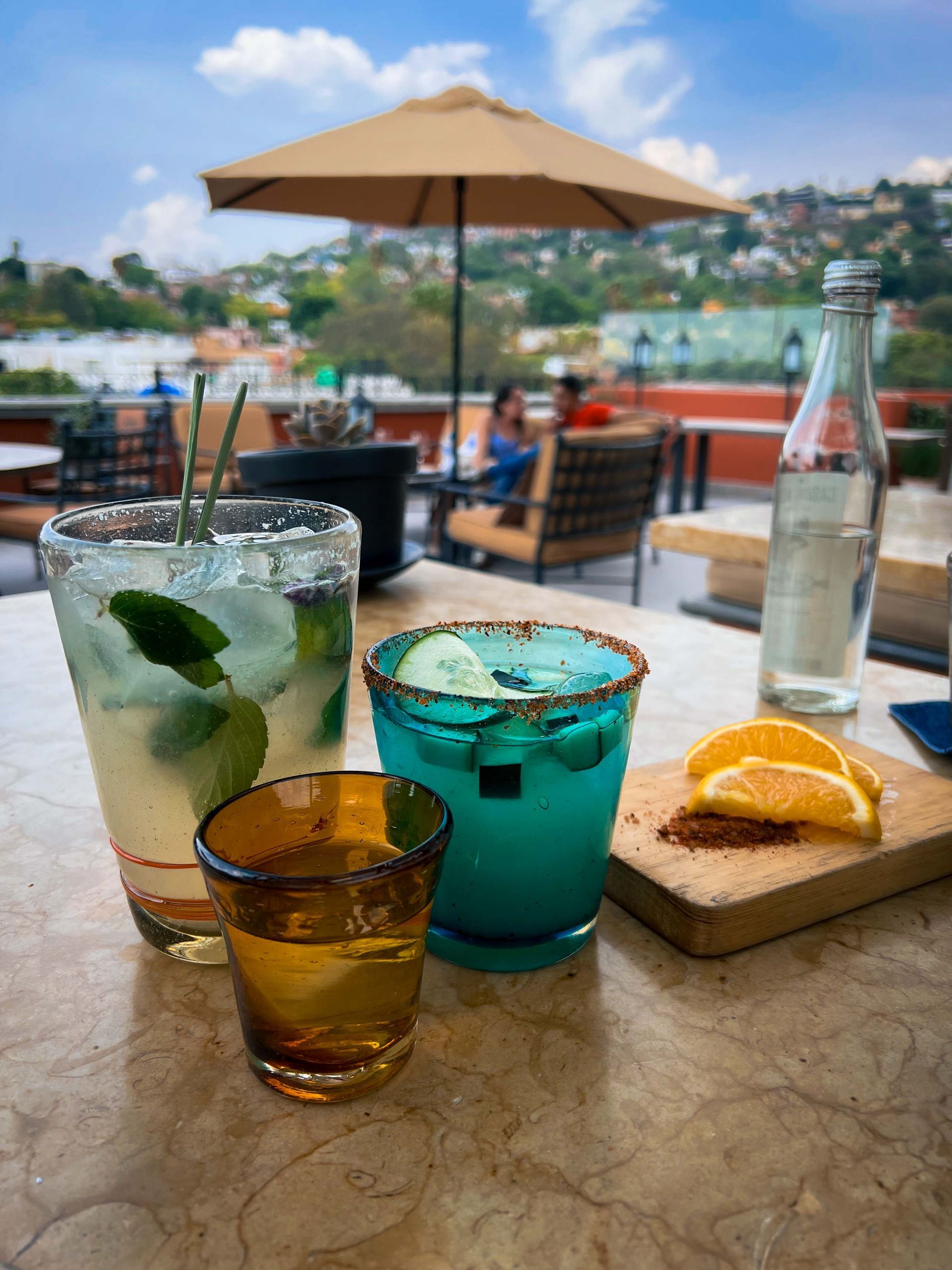 Three drinks are sitting on a table with an umbrella in the background in San Miguel de Allende