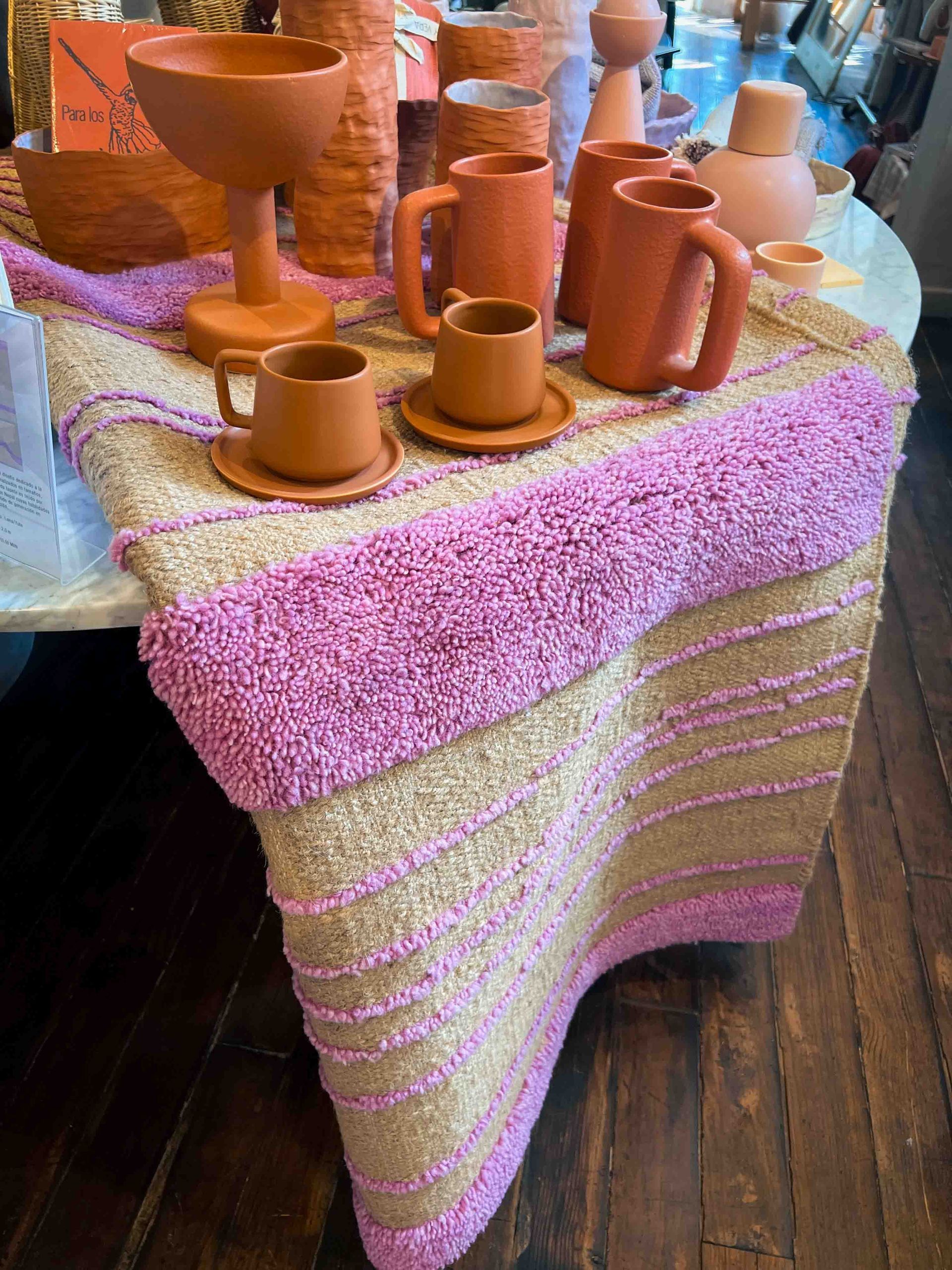 A table with a pink table runner and a bunch of mugs on it.