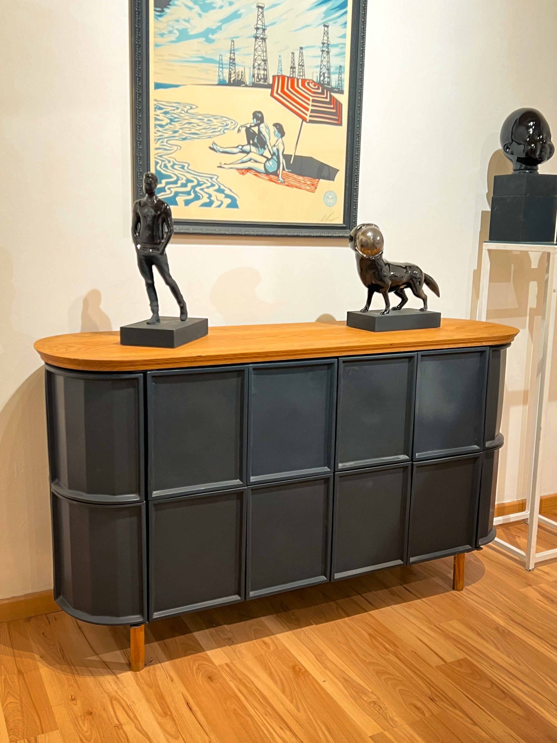 A dresser with two statues on top of it and a painting on the wall.