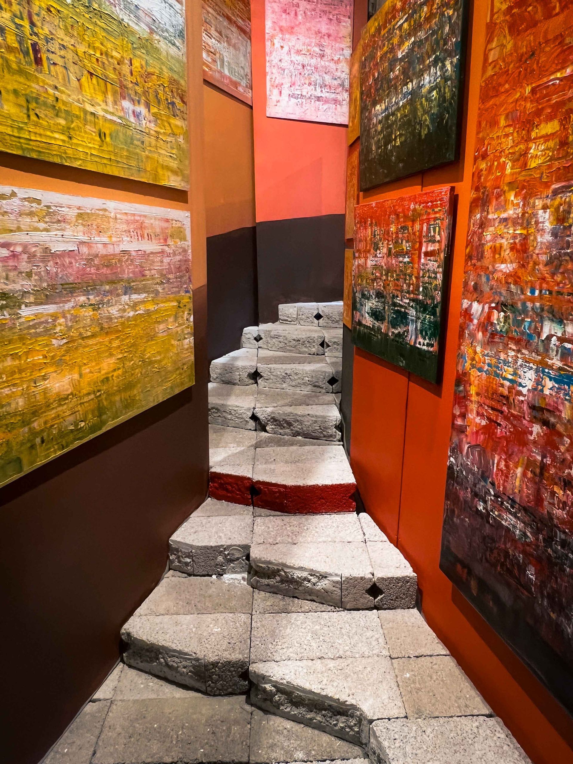 A narrow hallway with stairs and paintings on the wall