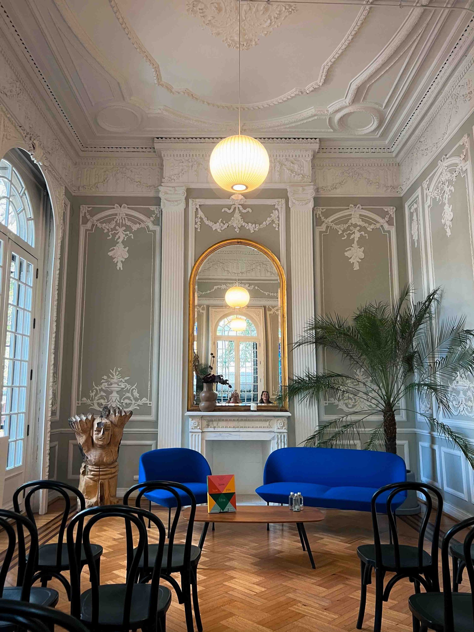 A living room with a blue couch , chairs , a table and a mirror.