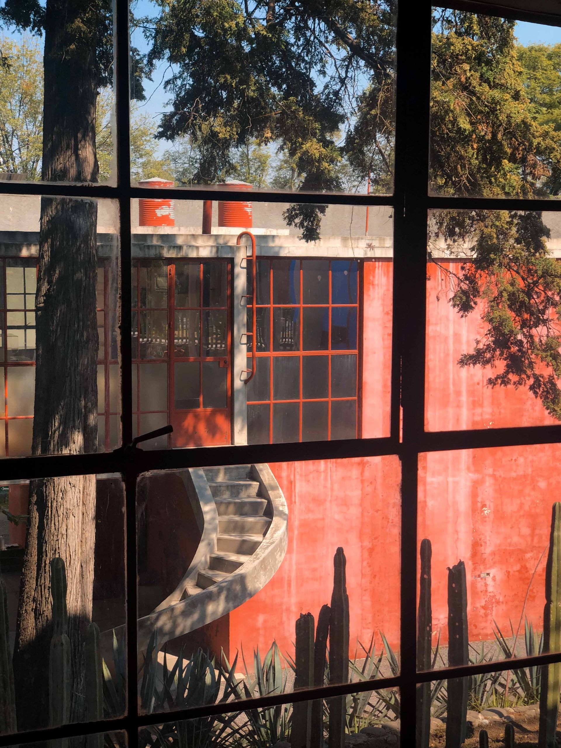 A red building with a spiral staircase is seen through a window