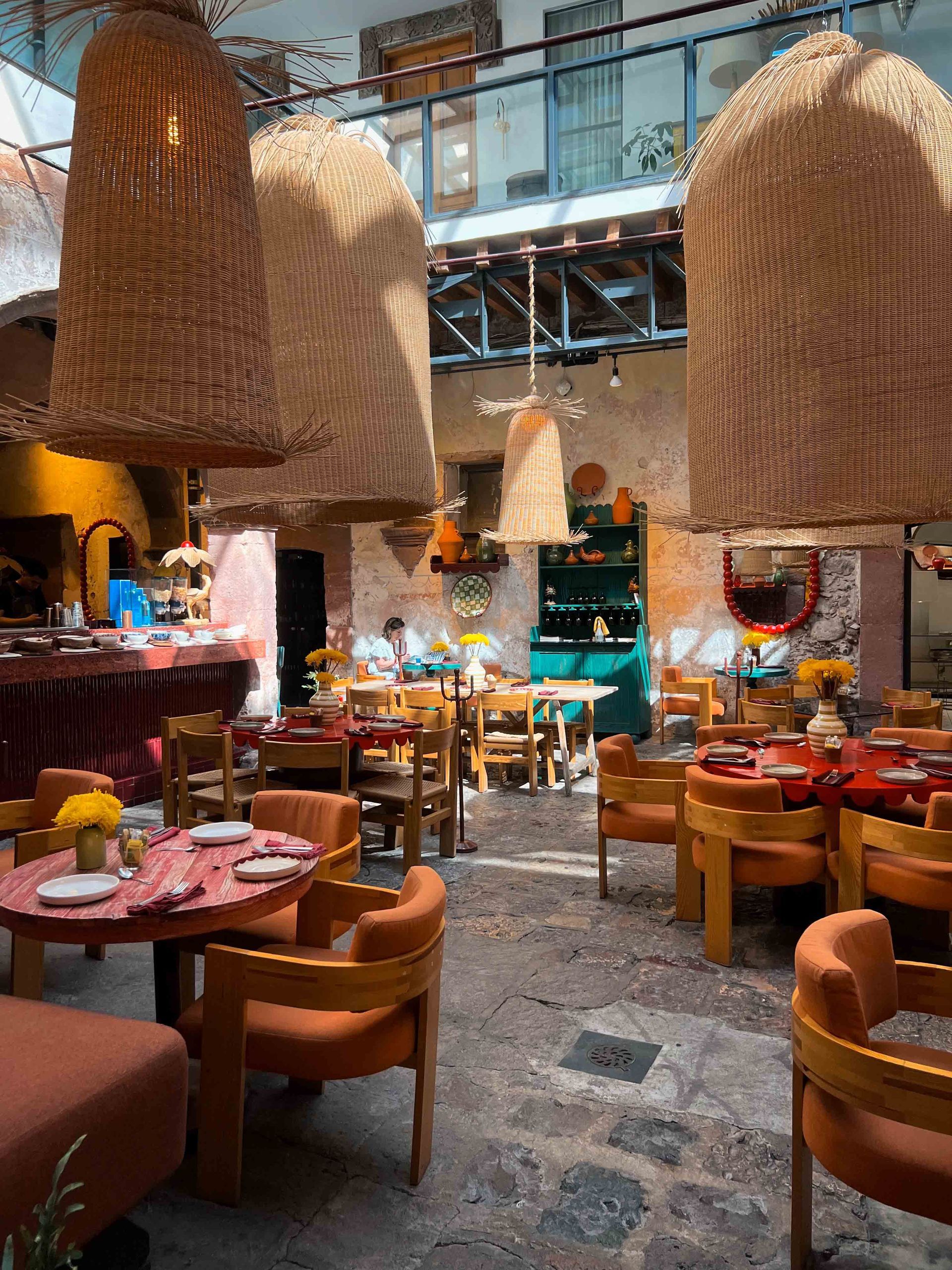 A restaurant in San Miguel de Allende with tables and chairs and wicker lamps hanging from the ceiling.