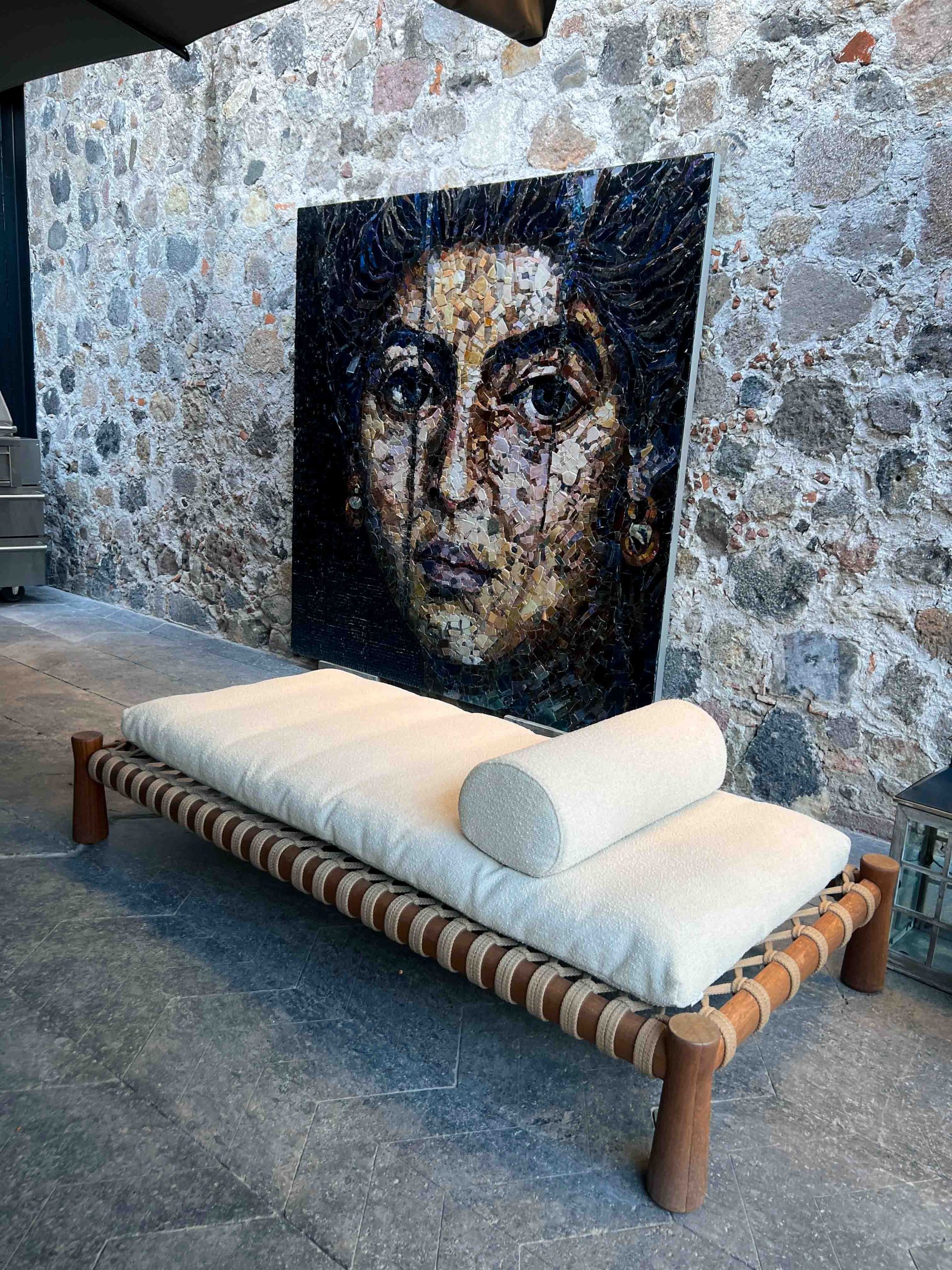 A painting of a woman 's face is behind a day bed.