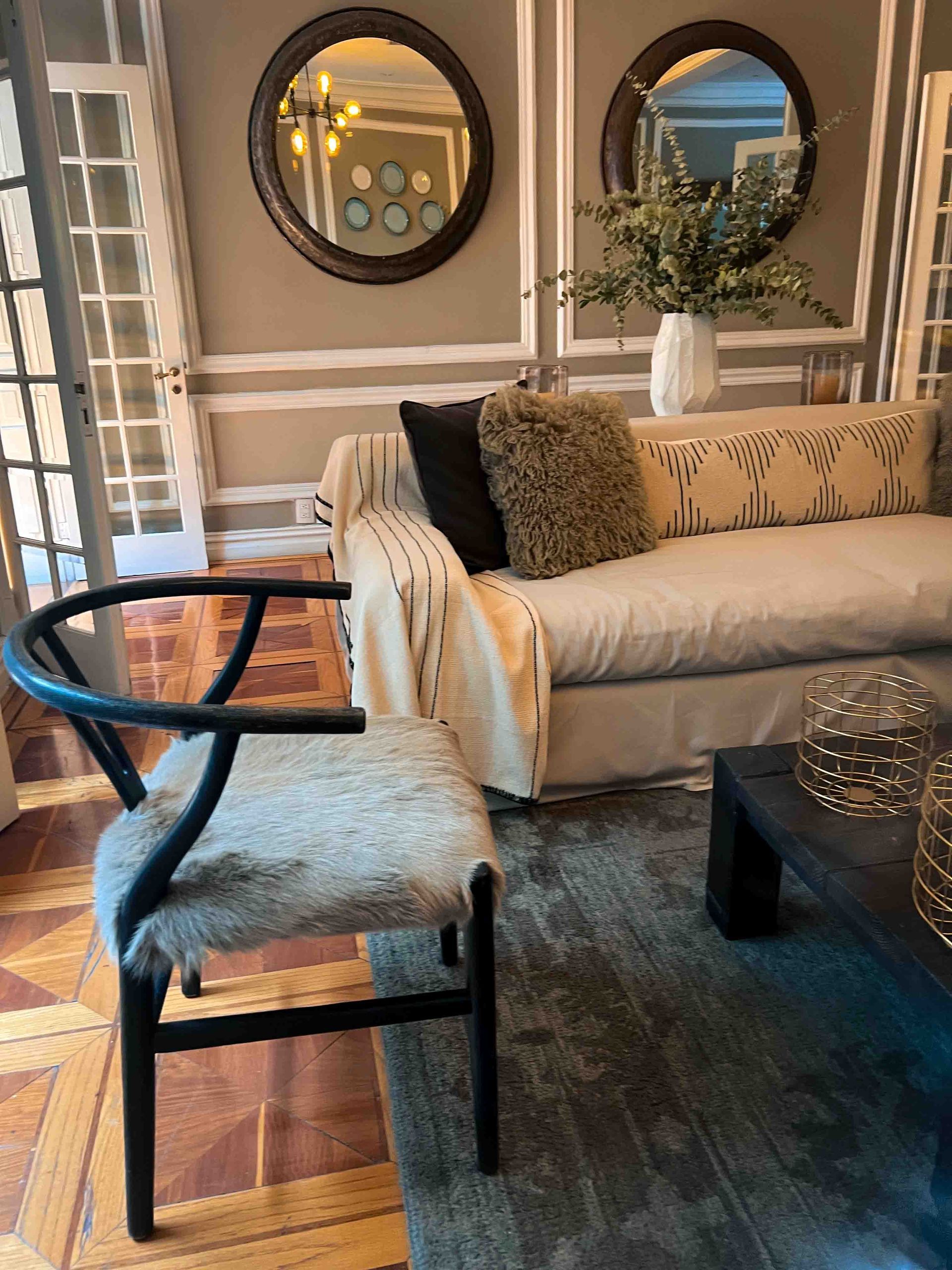 A living room with a couch , chair , coffee table and two mirrors.