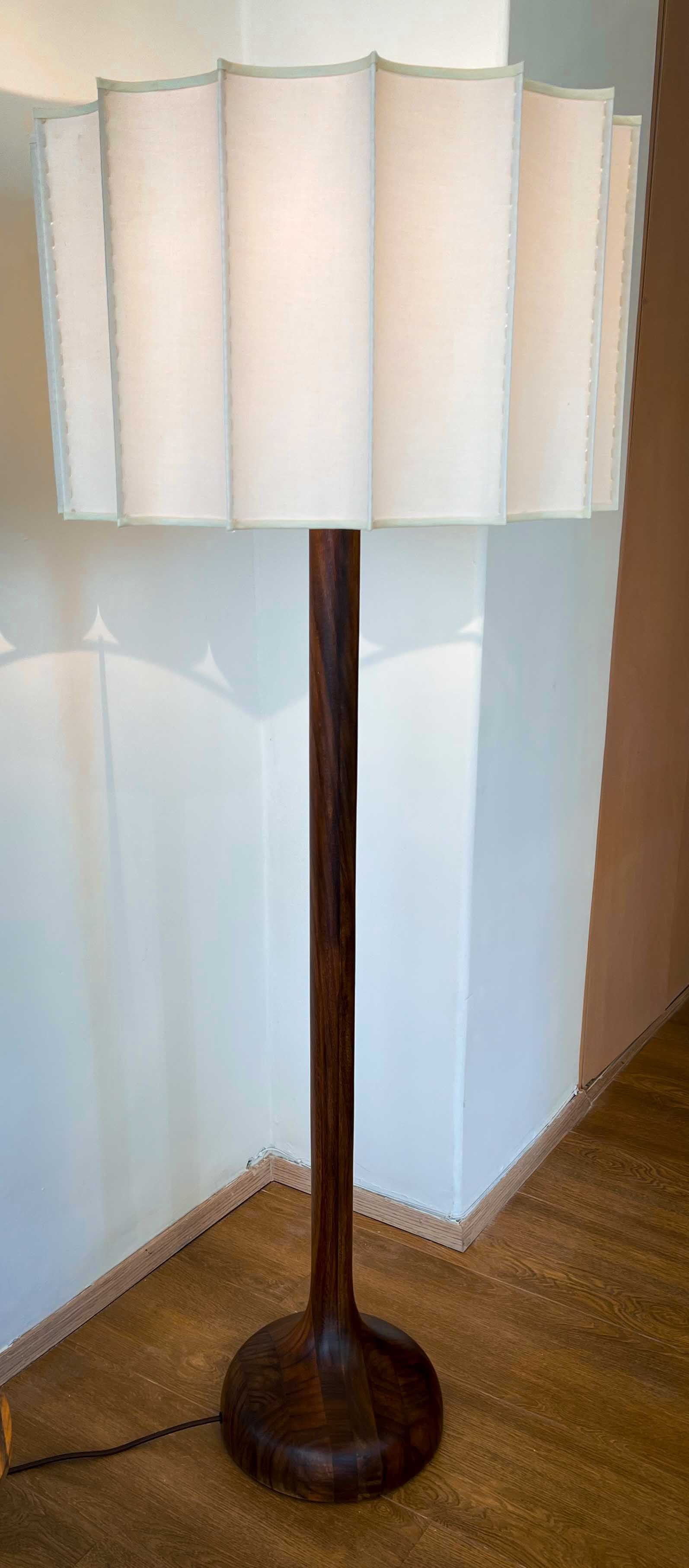 A lamp with a white shade is sitting on a wooden floor next to a wall.
