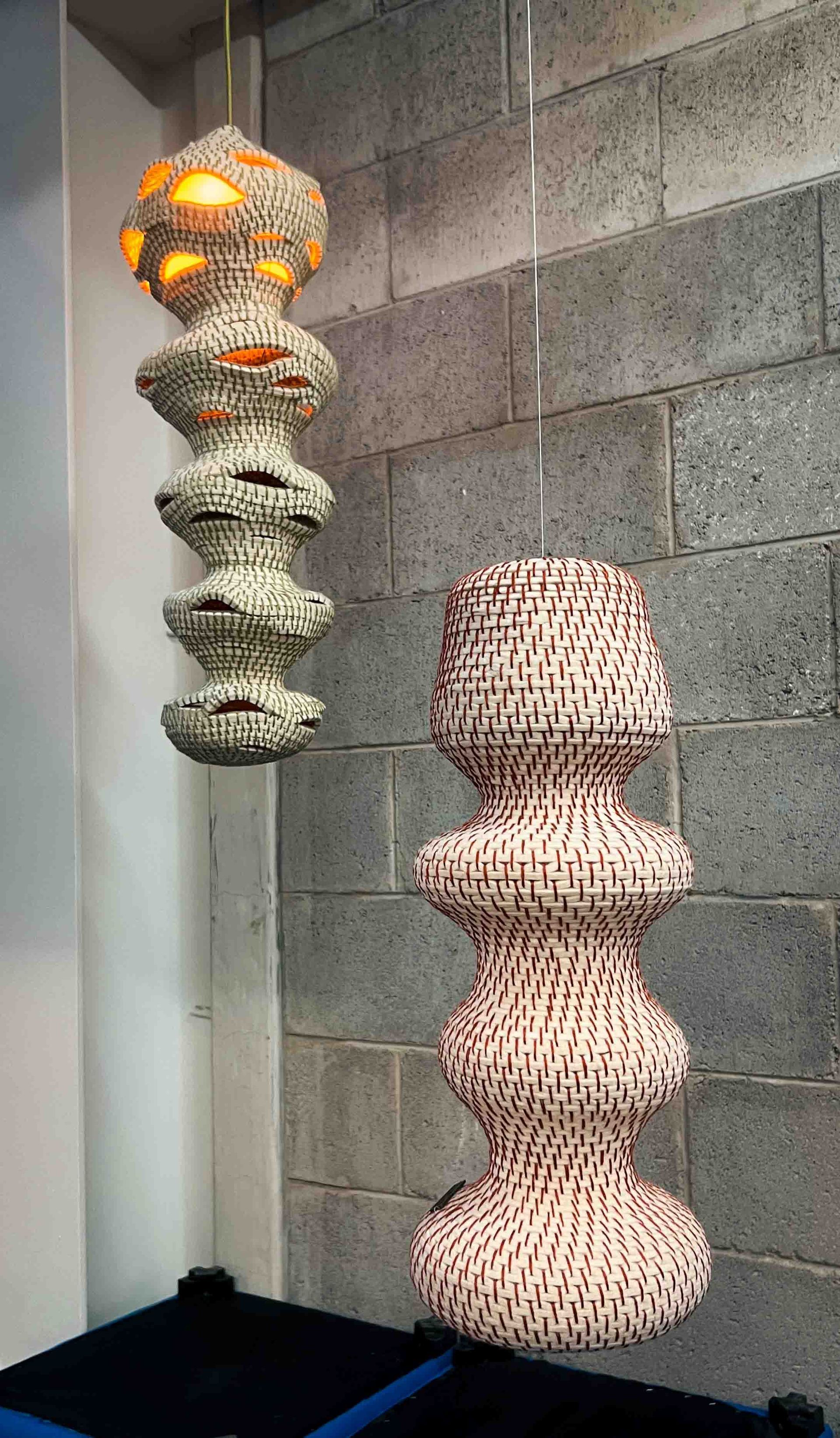 Two sculpture lamps are hanging from the ceiling in front of a brick wall.