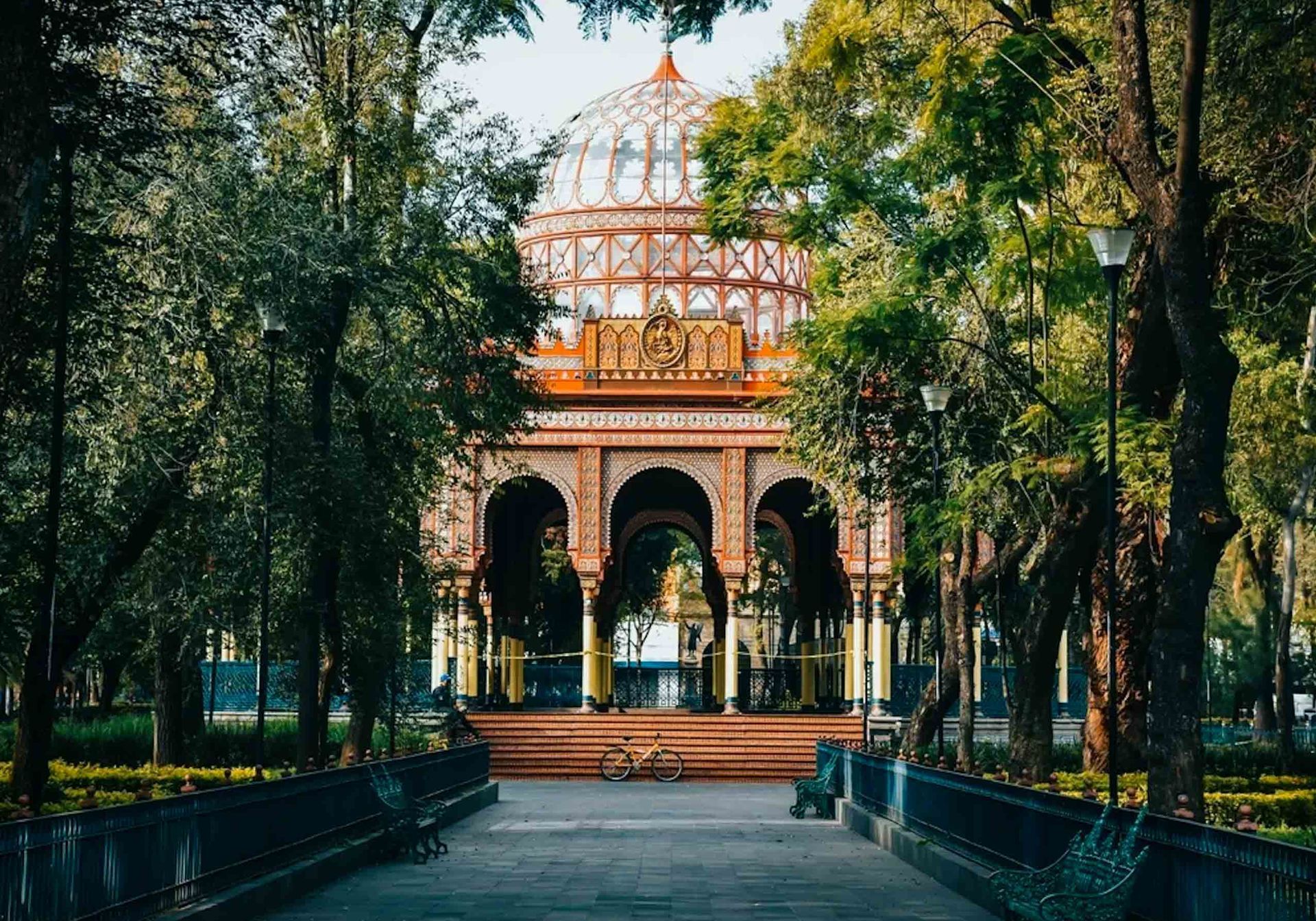 A building in a park in Mexico City with trees and benches in front of it