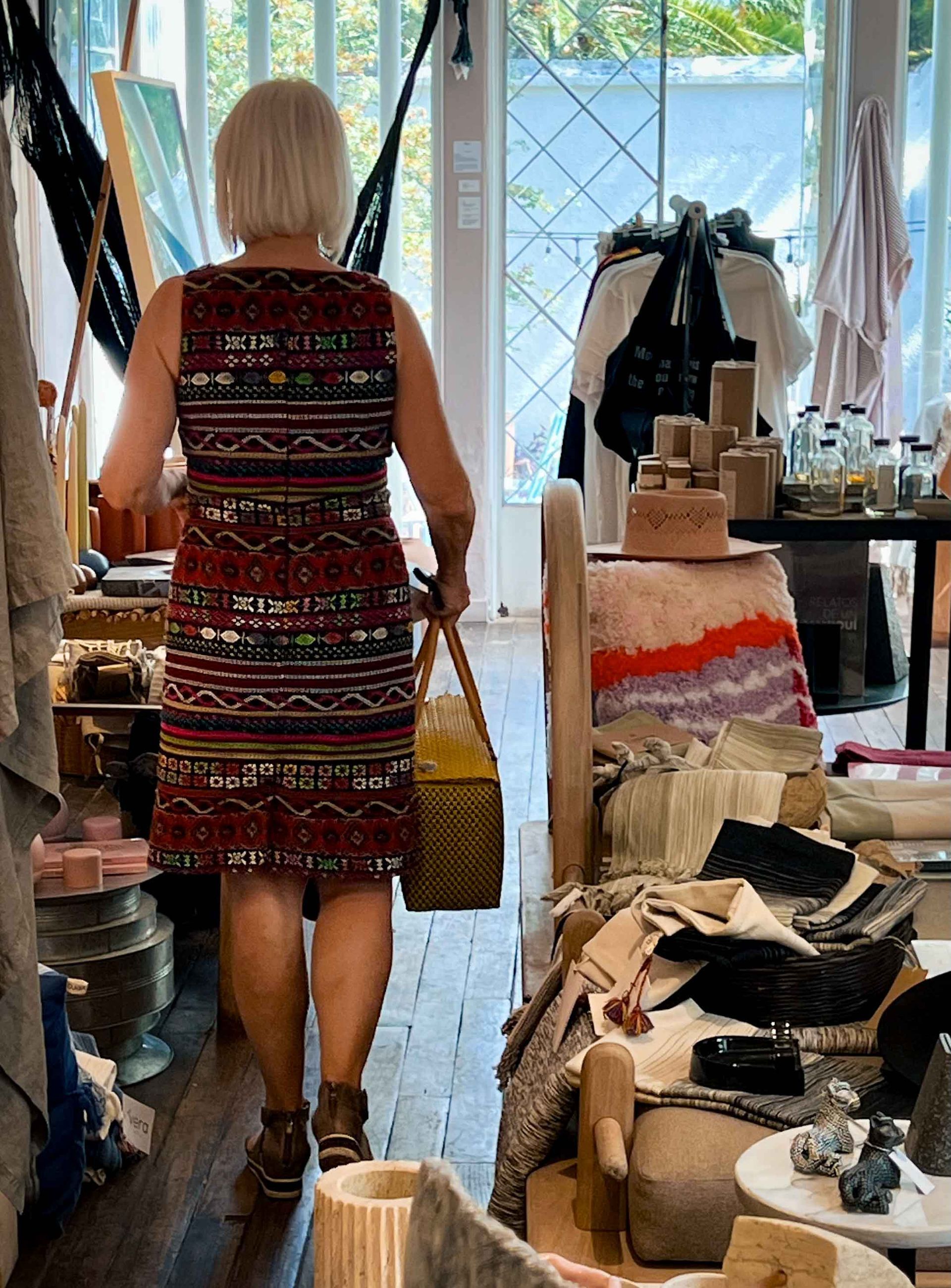 A woman in a dress is walking through a store holding a basket.