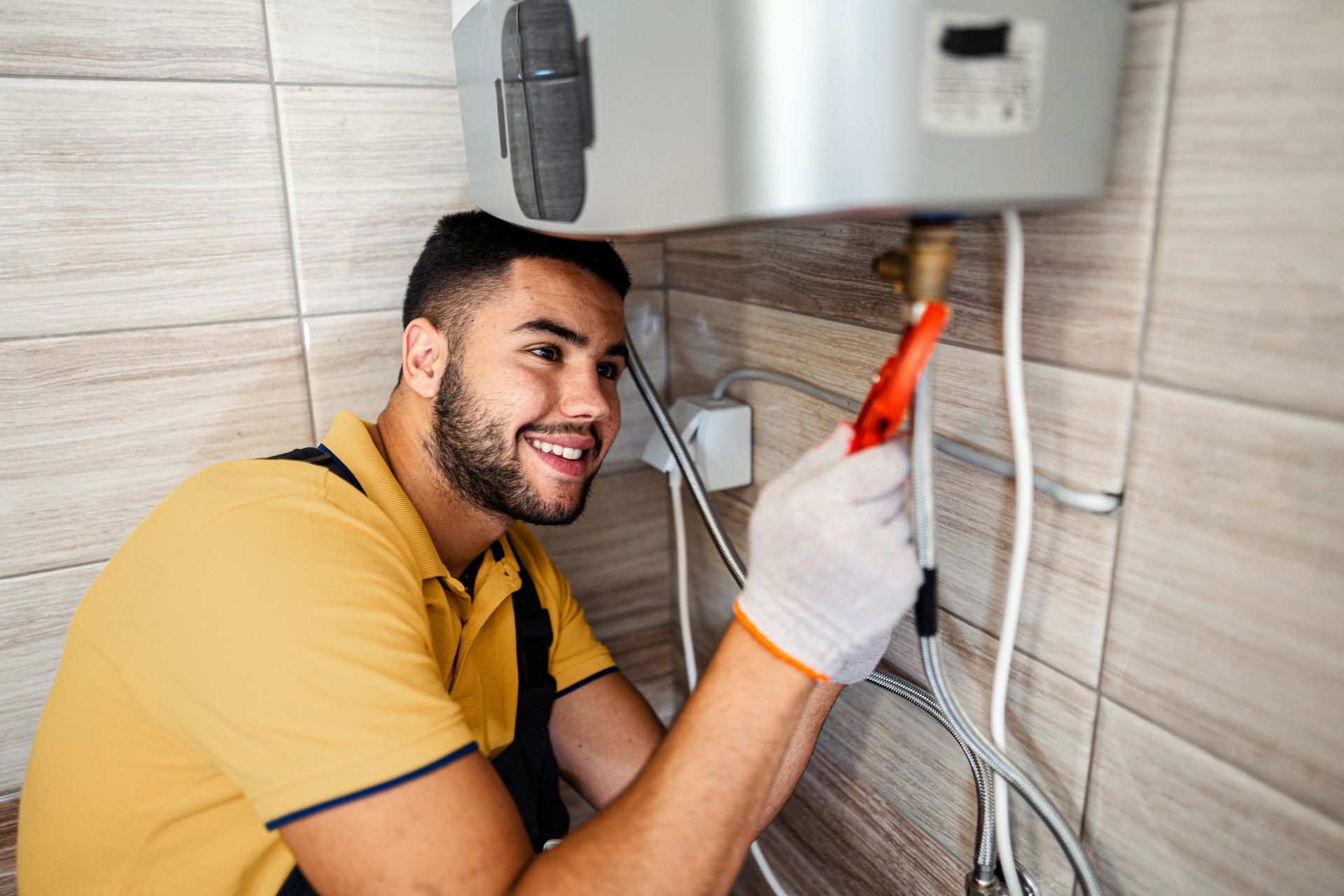 Smiling plumber adjusts a water heater with a wrench, showcasing professional water heater install.