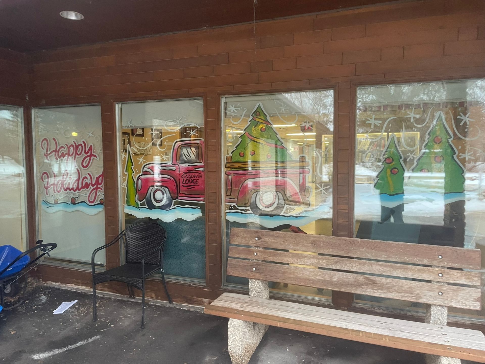 A wooden bench is in front of a building with christmas decorations on the windows.