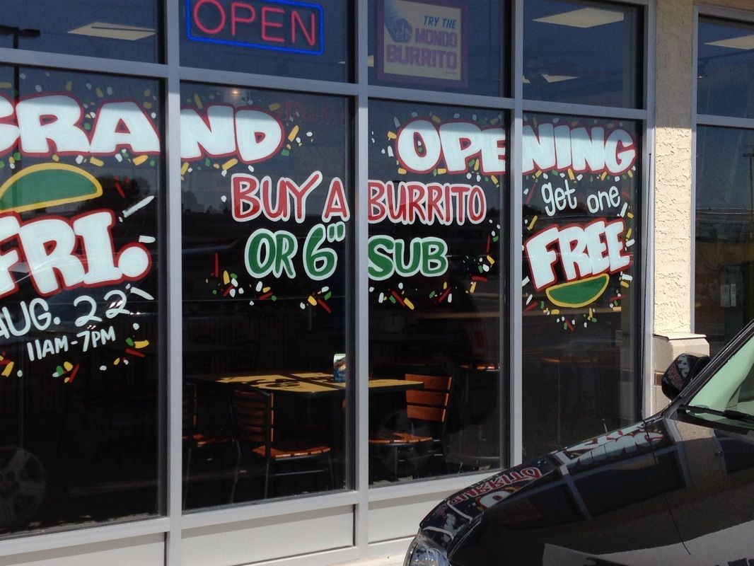 A car is parked in front of a restaurant that says buy a burrito or 6 sub