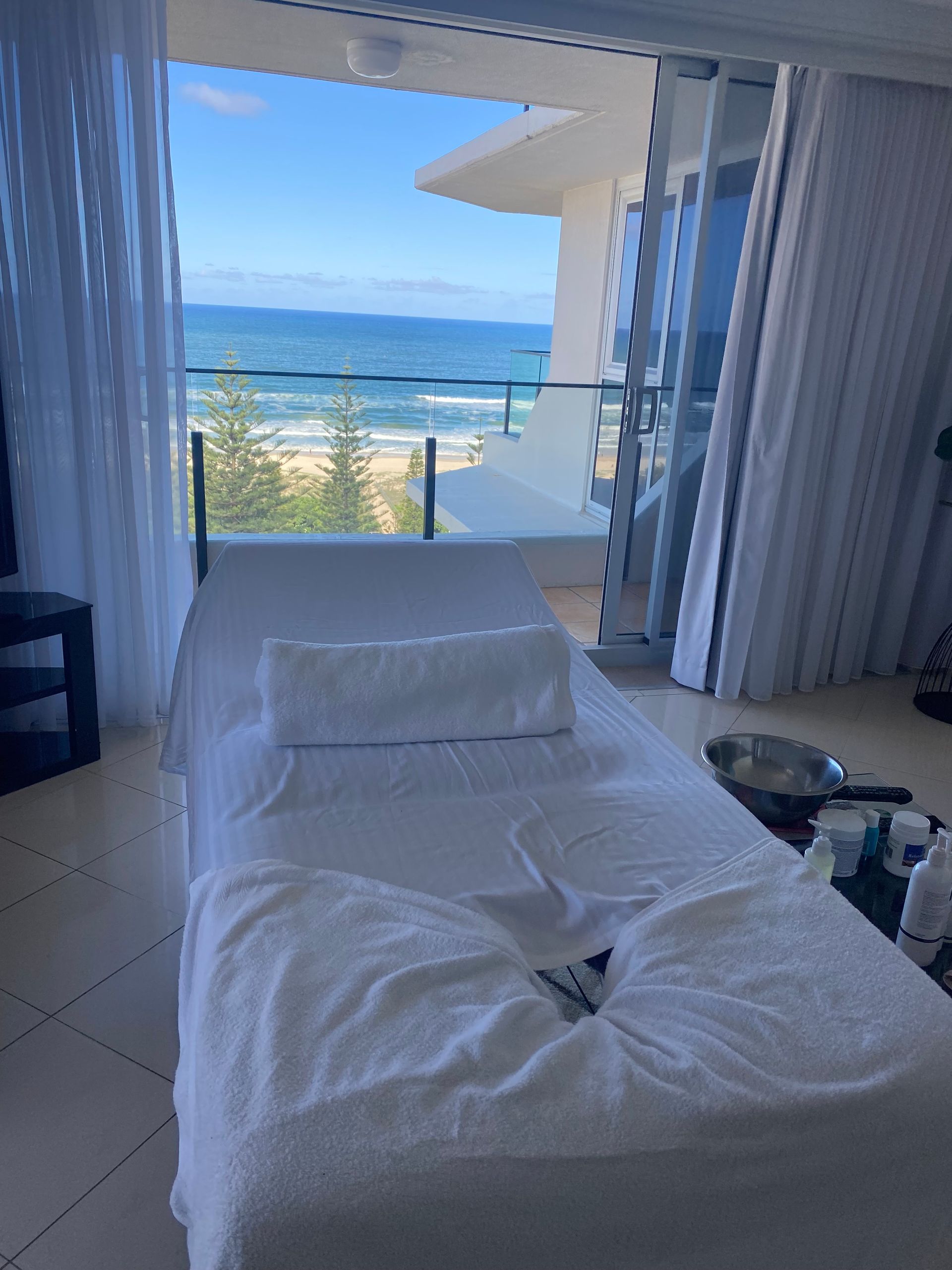 A Beauty Bed With White Sheets On It With A Window Showing The Ocean — Soul Good Beauty in Miami, QLD
